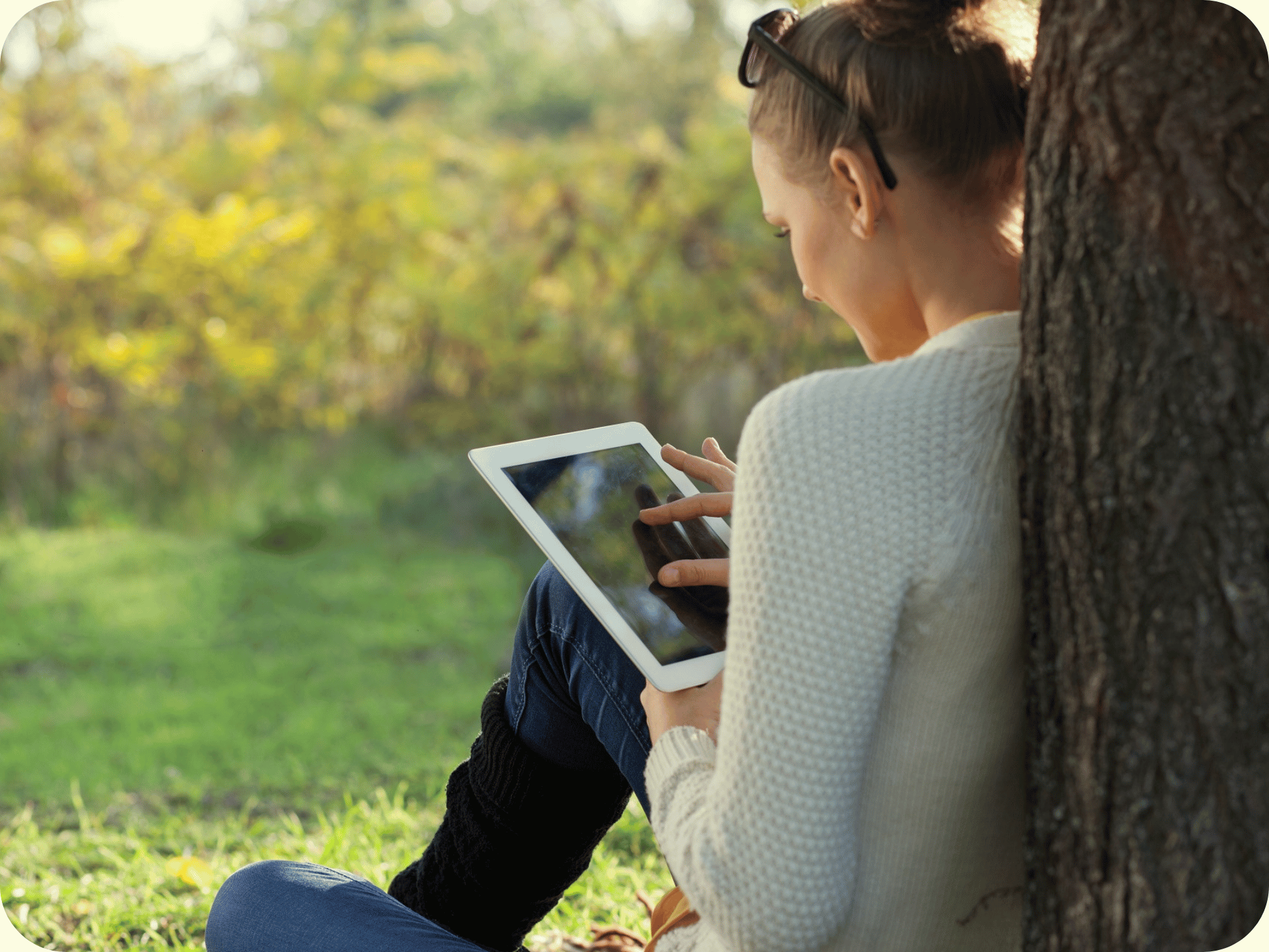Student sitting under a tree using a tablet to read an eBook in a natural setting