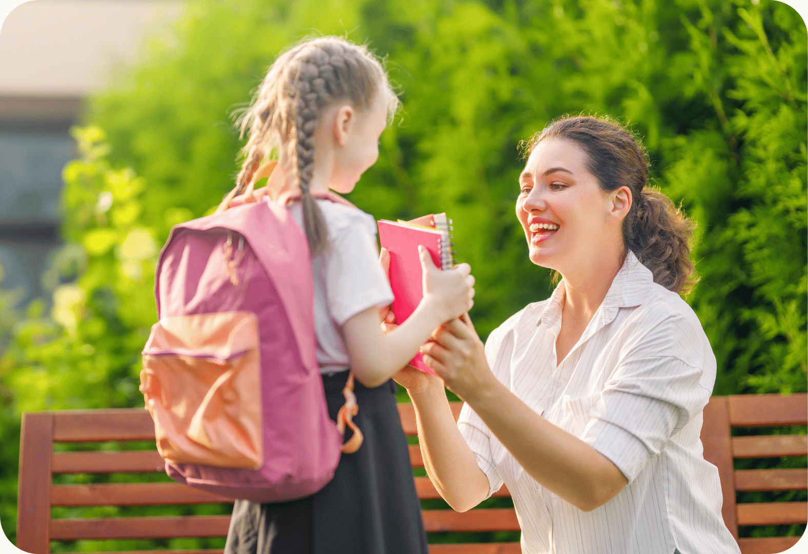 Young girl with braided hair receives school books from a smiling parent outside, highlighting parent-teacher collaboration in education.