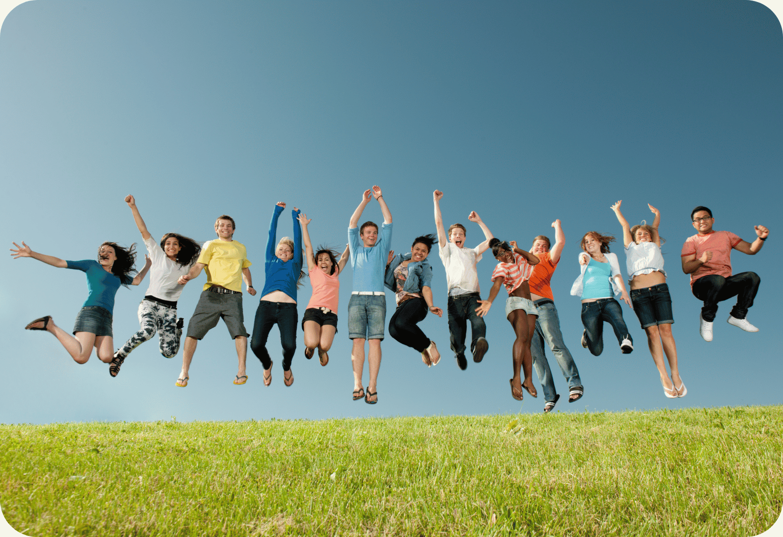 Diverse group of high school students jumping joyfully on a grassy hill under a clear blue sky, representing student engagement and wellbeing.