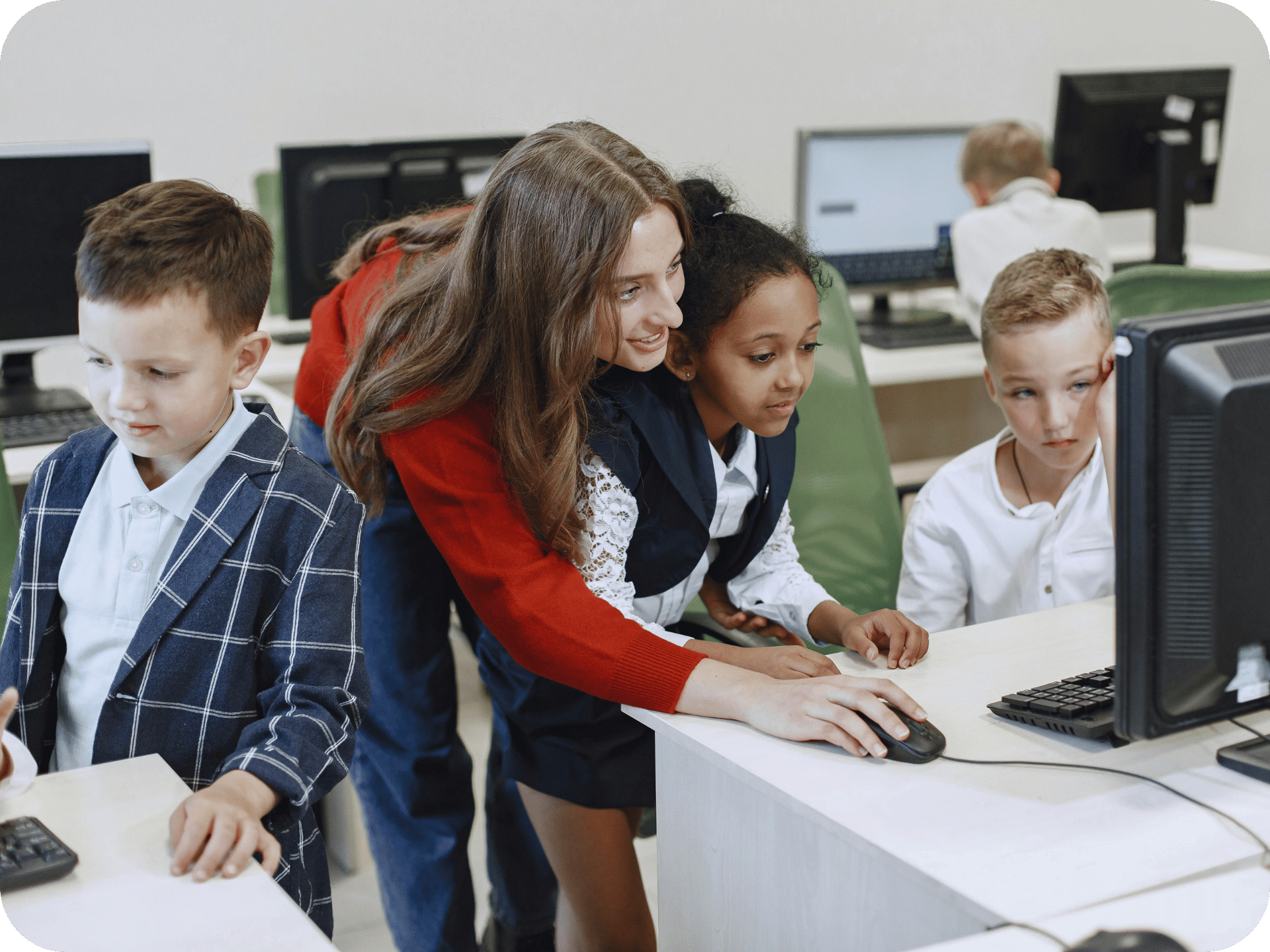 Teacher helping young students use ePlatform on desktop computers in a classroom.